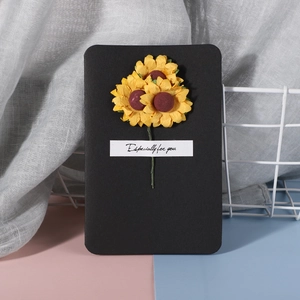 Detail of a black greeting card featuring handmade yellow sunflowers and a small label