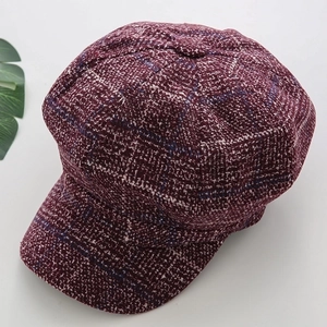 Detailed close-up of dark wine red plaid tweed texture on a stylish newsboy octagonal hat