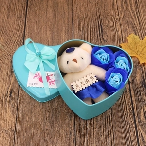 Blue heart-shaped metal gift box with soap roses and a plush bear on wood background