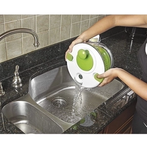 Manual plastic vegetable salad spinner with clear bowl and green strainer in kitchen sink