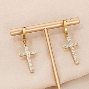 Detail shot of a golden cross earring with sparkling zircons on a pink velvet stand