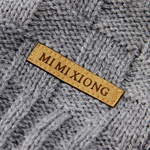 Gray knitted baby blanket with soft texture and a premium brown leather brand label