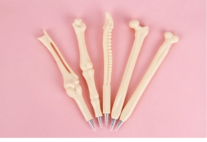 Detailed view of five bone-shaped ballpoint pens with silver metal tips on pink backdrop