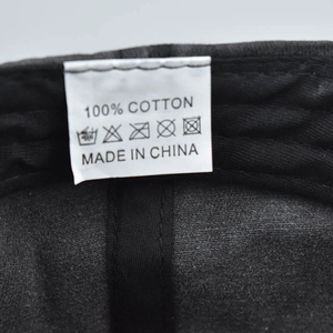 Detail of 100% cotton wash label on black baseball cap showing care symbols and origin