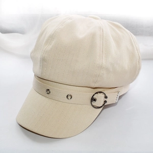Detail of beige octagonal cap showing herringbone texture and metal eyelet belt