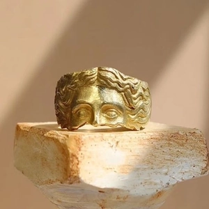 Artistic gold Venus face relief open ring displayed on natural textured stone background