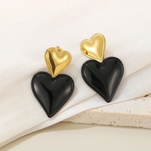 Fashionable black and gold double heart drop earrings on textured white stone background