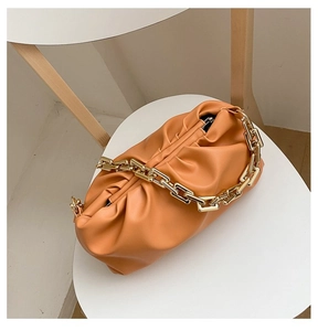 Close-up of orange cloud bag in soft PU leather with chunky gold chain strap on table