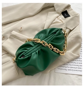 Detail of dark green pleated cloud bag with chunky gold chain strap on a beige blazer