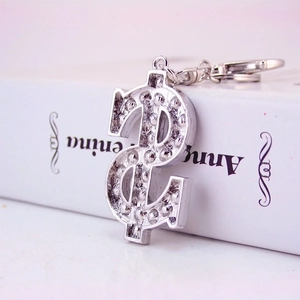 Silver dollar sign keychain with sparkling crystals and standard ring on a book