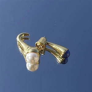 Pendientes bañados en oro con perla blanca y piedra azul sobre superficie reflectante azul