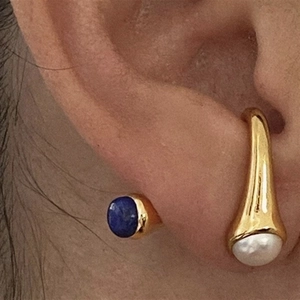 Elegantes pendientes dorados con piedra natural azul y perlas puestos en la oreja