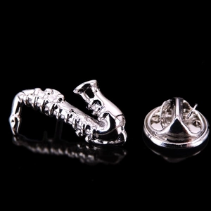 Macro detail of silver saxophone lapel pin with butterfly clutch on black mirror