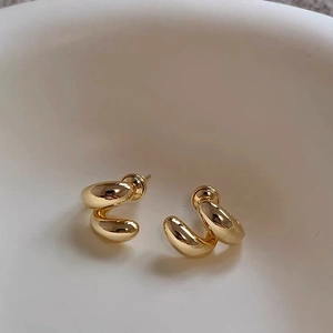 Detailed close-up of golden geometric spiral earrings on a beige ceramic surface