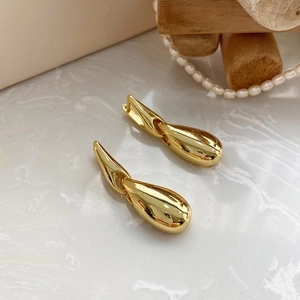 Detail view of gold teardrop earrings with a polished finish on marble surface
