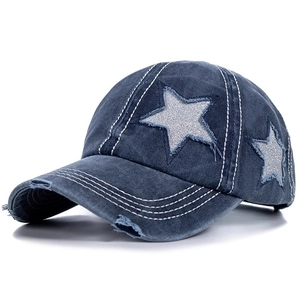 Detailed view of dark blue distressed denim baseball cap with silver sequin star patches