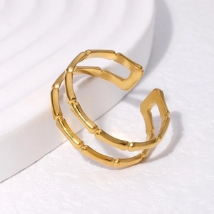 Dettaglio dell'anello regolabile in oro a forma di bambù su base bianca materica