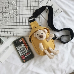 Détail du sac de poitrine en toile jaune avec ours en peluche et large sangle noire