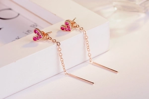 Macro shot of long golden dangle earrings featuring pink heart charms and sparkling stones