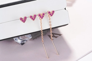 Macro detail of rose gold heart earrings with pink crystals and long chain tassels