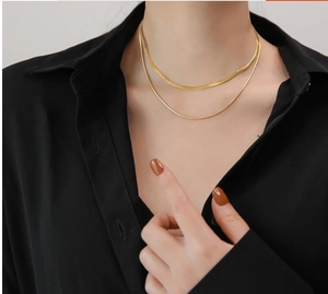 Dubbellaagse gouden slangenschakel en fijne ringketting op een zwart overhemd
