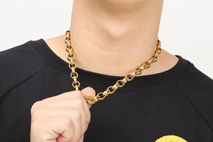 Detail of chunky gold stainless steel chain necklace worn by male model on black t-shirt