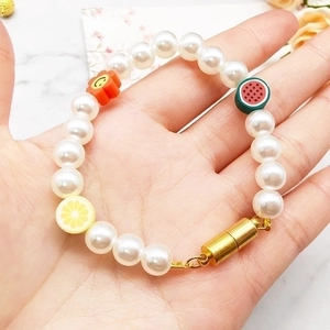 Detail of beaded pearl bracelet with gold magnetic clasp and colorful fruit charms