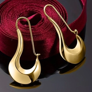 Elegant gold drop earrings with a fluid U-shape design over deep red ribbons