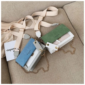 Detail of blue and green matte crossbody bags with golden chains on a beige sofa