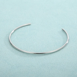 Polished silver minimalist open bangle shown on a light blue textured surface