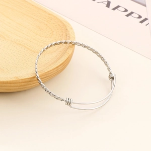 Close-up of a silver twisted cable bangle with adjustable sliding knot on wood tray