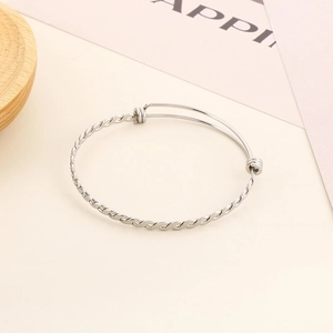 Macro detail of adjustable twisted silver stainless steel bangle on a minimalist background