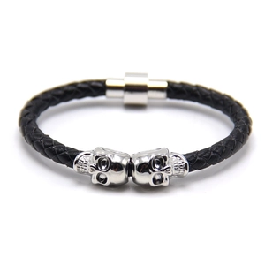 Detail of black braided leather bracelet featuring silver skull beads and magnetic clasp