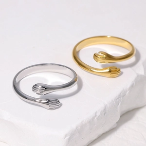 Detailed view of gold and silver hugging hands open rings on textured stone background