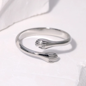 Polished stainless steel hugging hands open ring on a minimalist stone background