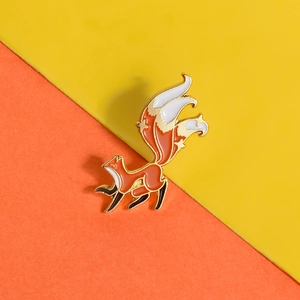 Close-up of cute orange fox enamel brooch with gold-tone edges on bright background