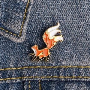 Cute orange and white fox enamel pin with gold edges on a blue denim jacket pocket