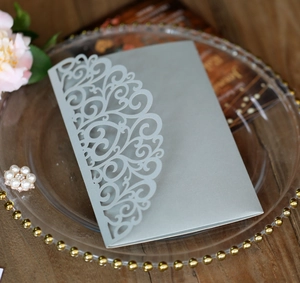 Intricate laser-cut silver pearl paper invitation sleeve on a decorative glass tray
