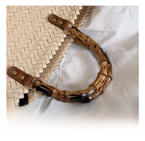 Détail d'un sac en paille tressée avec poignée en bambou et rivets en cuir sur tissu blanc