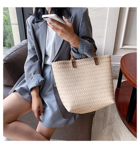 Gros plan du sac cabas en paille tressée beige avec anses en cuir marron et rivets