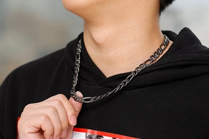 Close-up of a men's vintage grey stainless steel Figaro chain necklace worn by a model