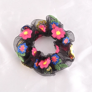 Close-up of black mesh scrunchie featuring colorful floral embroidery on white fabric