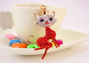 Detail of red rhinestone cat keychain with golden crown leaning on white ceramic cup