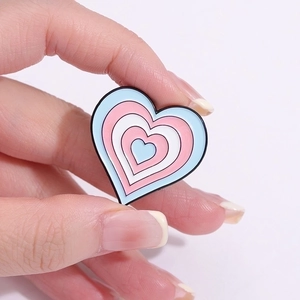 Transgender flag colors heart enamel pin held by hand against a pink background