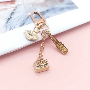 Chic gold keychain featuring lipstick, lip, and quilted handbag charms on a pink surface