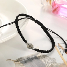 Detalle de pulsera de cuerda negra trenzada con colgante de sol grabado en plato blanco