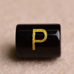 Macro shot of a black cylindrical bead with a golden letter P for DIY jewelry making