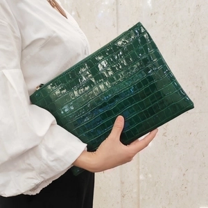 Dark green crocodile embossed clutch bag with shiny finish held by a model