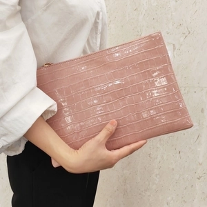 Pink crocodile texture envelope clutch bag shown held against marble background
