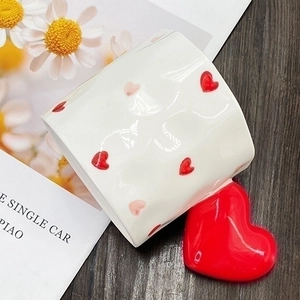 Detail of a ceramic mug with red heart patterns and a bold red heart-shaped handle on a table
